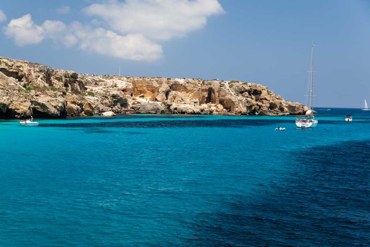 Scorcio della spiaggia di Cala Rossa con mare cristallino e scogli, turisti che si godono il sole, colori vivaci