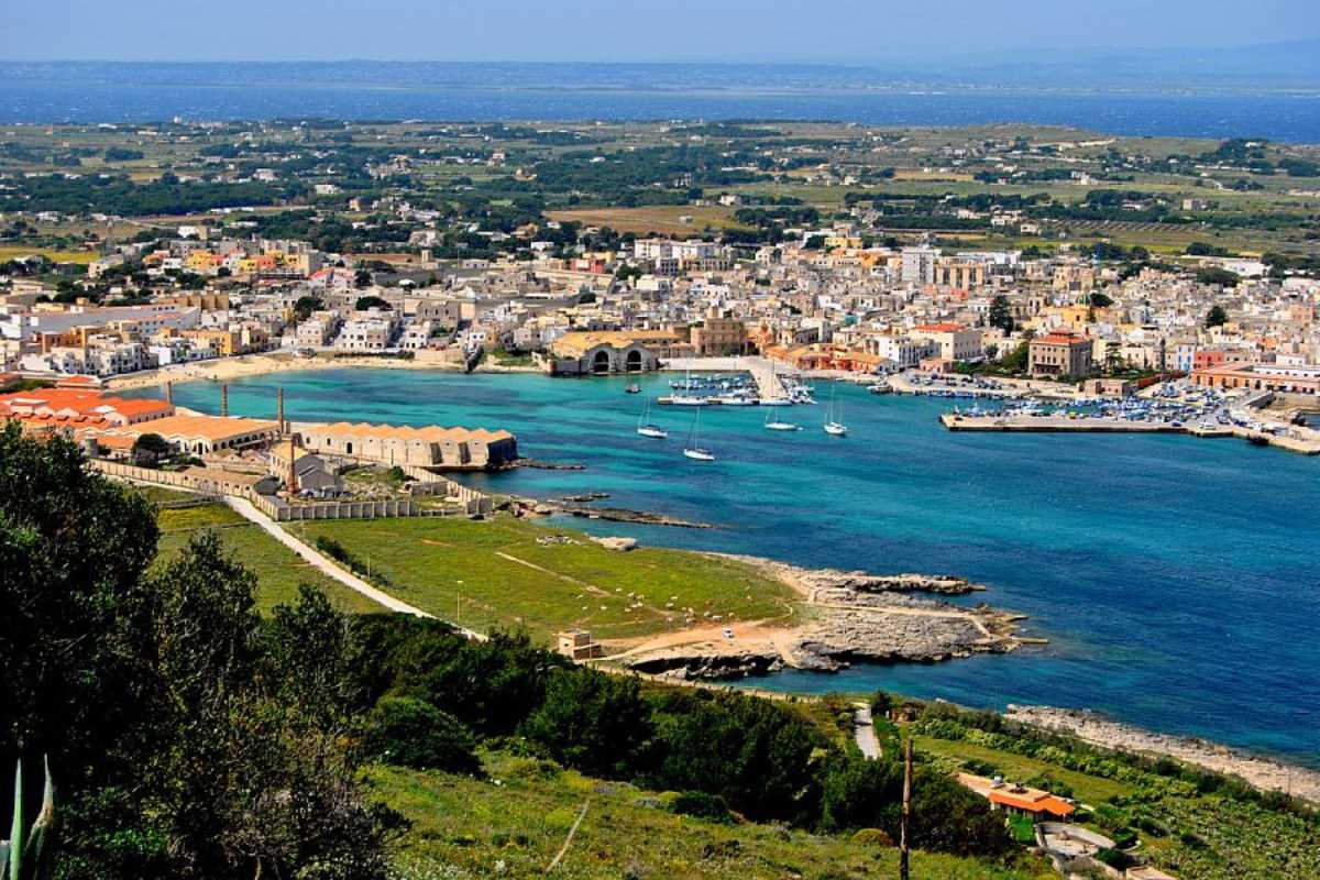 Famiglia felice con bambini che gioca sulla spiaggia sabbiosa di Favignana, acqua cristallina, sfondo di barche colorate e paesaggio mediterraneo